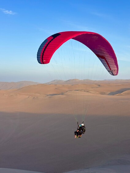A person paragliding over a desert landscape with sand dunes. 2