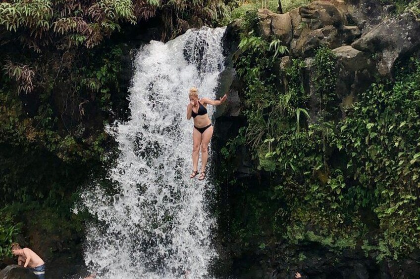 A person jumping off a waterfall surrounded by lush greenery. 4