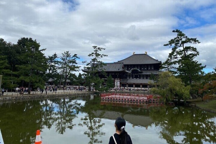 A traditional Japanese building with a reflection in a pond, surrounded by trees and a cloudy sky. 2