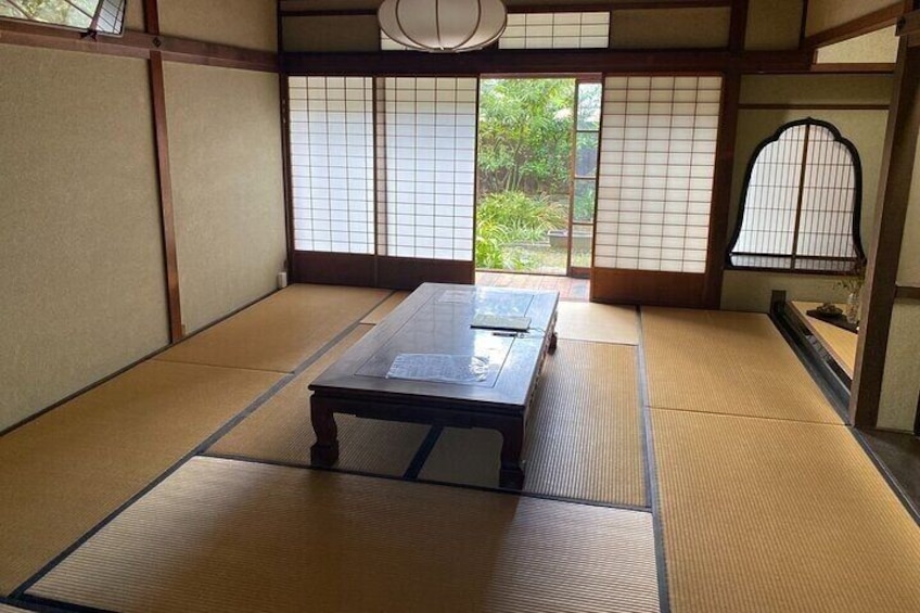A tatami mat room with a low table, sliding doors, and a view of greenery outside. 3