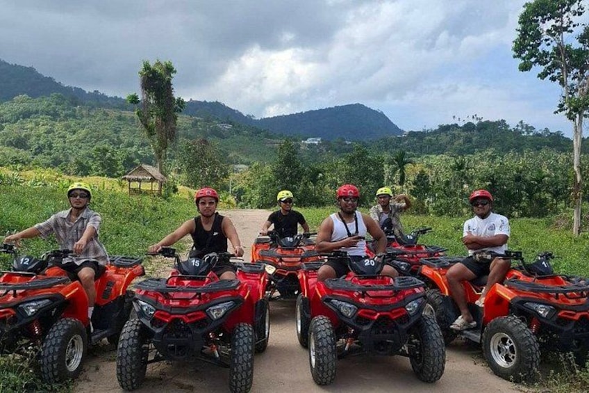 Five people on ATVs in a rural setting with hills in the background. 3