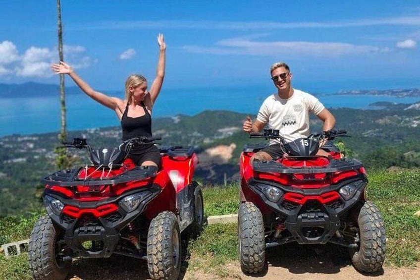 Two people on red ATVs with a scenic landscape in the background. 1