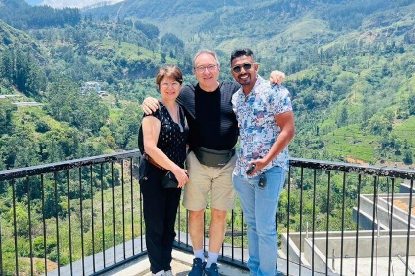 Three people standing on a balcony with a mountainous landscape in the background. 2