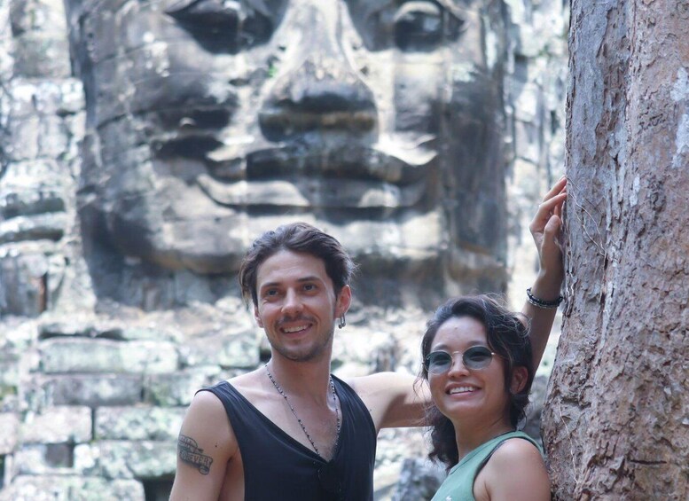A person touching a tree trunk with a large stone face in the background. 2