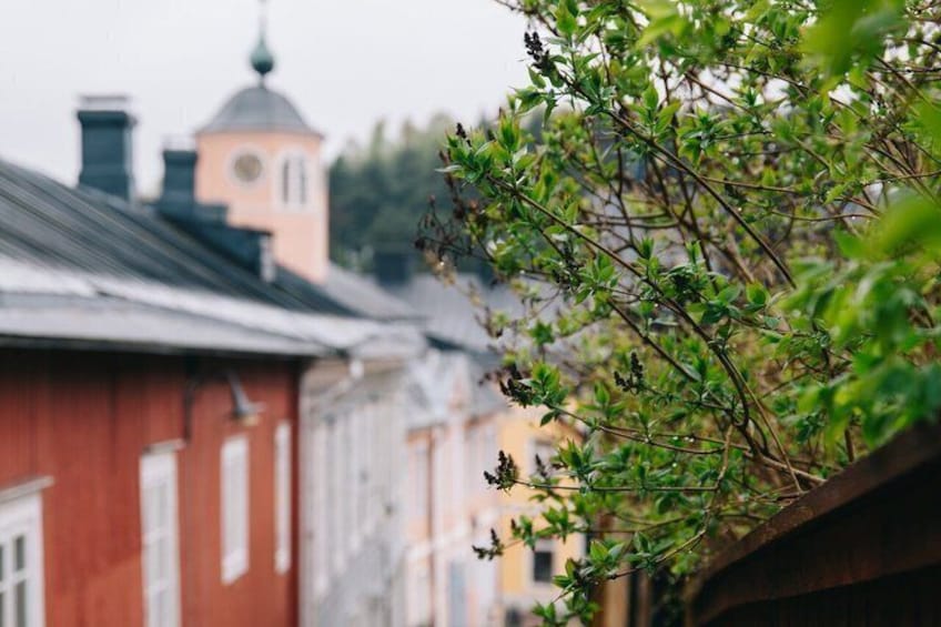 A red building with a clock tower, a tree branch with green leaves, and a blurred background of other buildings. 3