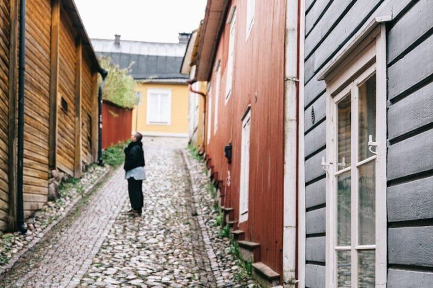 A narrow cobblestone alley flanked by wooden buildings, a person walking down the path. 5