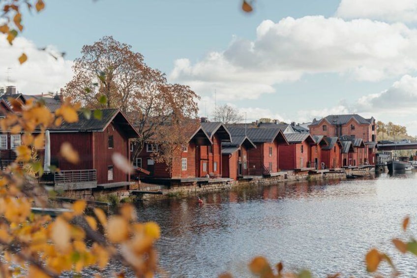 A row of red wooden buildings by a calm river. 1