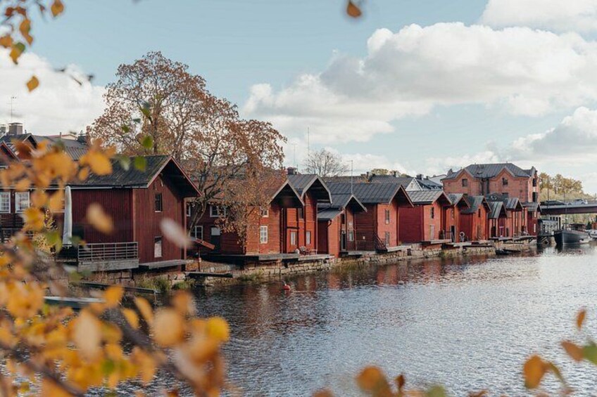 A row of red wooden houses by a calm river. 1