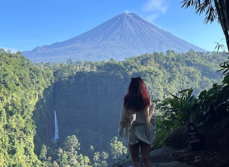 A woman standing with a view of a volcano and a waterfall. 1