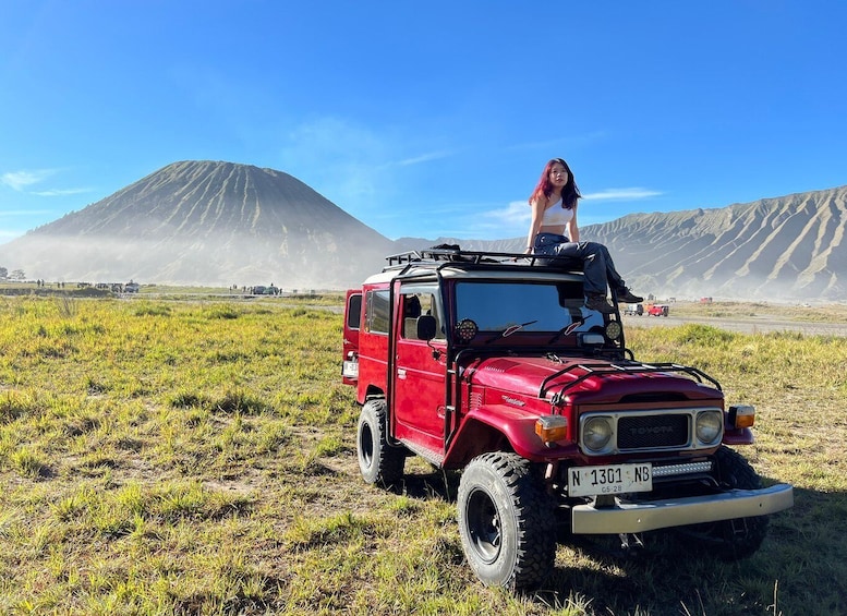 A red off-road vehicle parked in a grassy field with a mountain in the background. 4