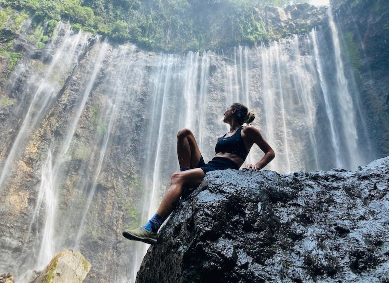 A person sitting on a rock with a waterfall in the background. 5