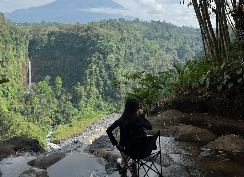 A person sitting on a chair overlooking a lush valley with a waterfall and dense forest. 3