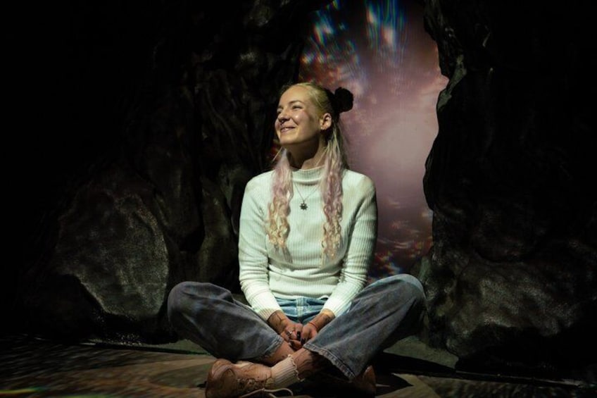 A person sitting cross-legged in a cave-like setting with rocky walls. 2