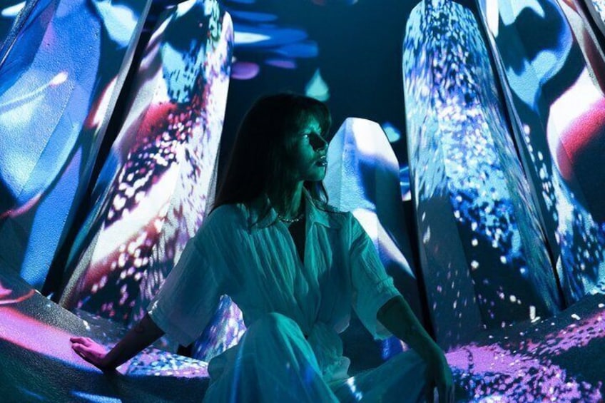 A person sitting in a futuristic setting with large, illuminated screens displaying abstract patterns. 5