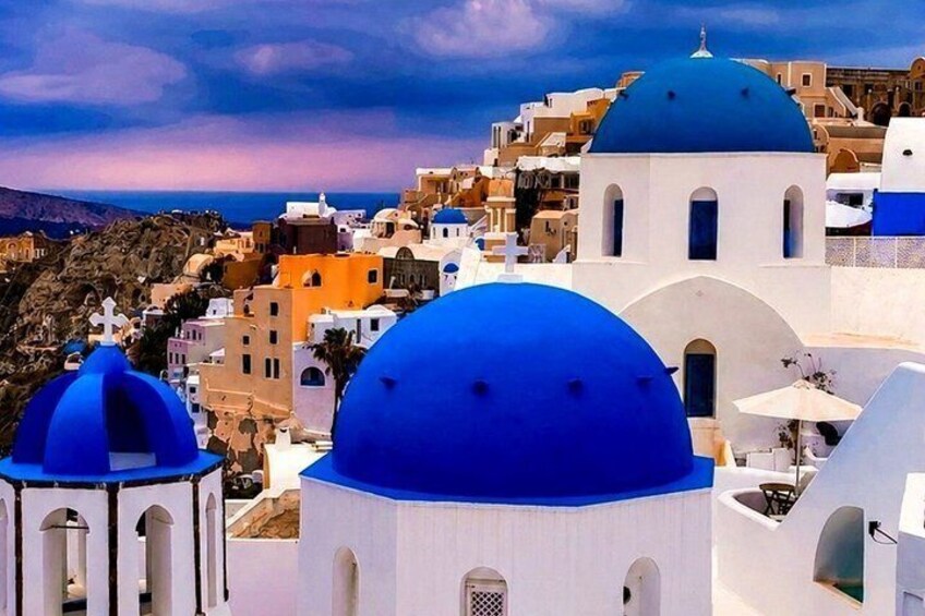 A coastal town with white and blue domed buildings, a mountainous backdrop, and a clear sky. 3