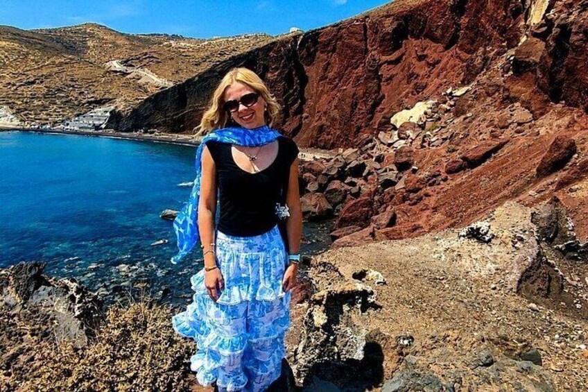A person standing on a rocky coastline with a clear blue sea and hills in the background. 5