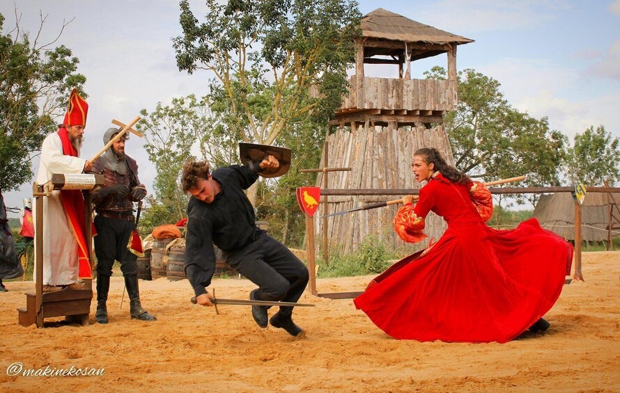 A medieval reenactment with actors in period costumes, a wooden structure, and a sandy ground. 4