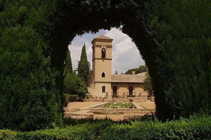 Un edificio histórico con un campanario, rodeado de abundante vegetación y un jardín cuidado. 3