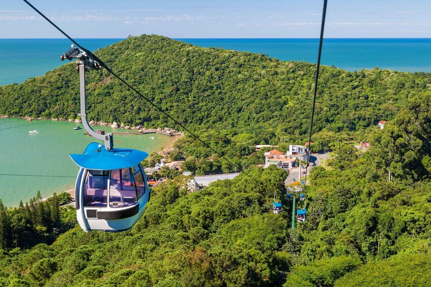 A cable car suspended over a lush green hillside with a view of the sea below. 4