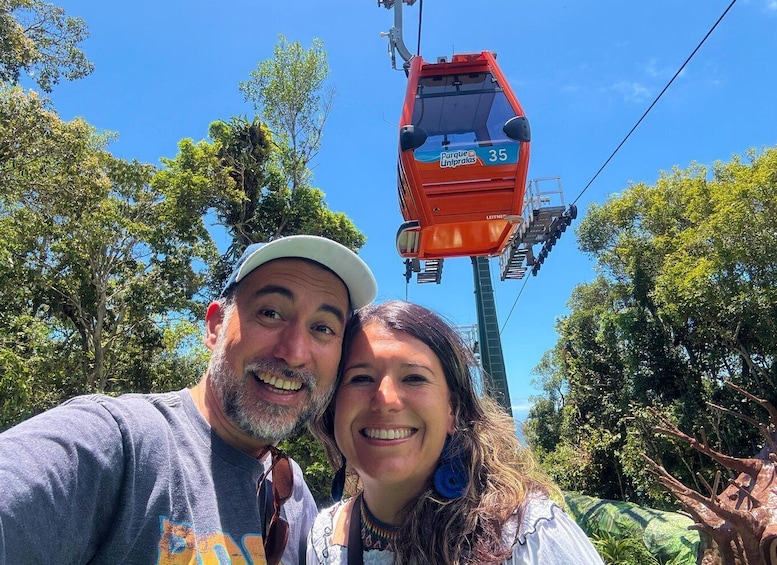A red cable car with the number 35, labeled 'Parque Uniprales,' against a backdrop of lush green trees and a clear blue sky. 2