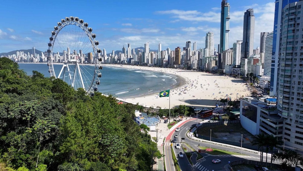 A coastal cityscape with a large Ferris wheel, a beach, and high-rise buildings. 1