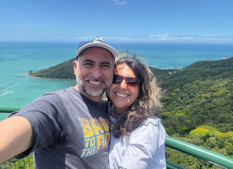A couple taking a selfie with a scenic view of a coastal landscape and a hill in the background. 3