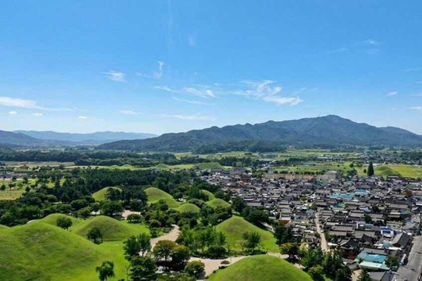 A town nestled in a valley with rolling green hills, a clear blue sky, and distant mountains. 2