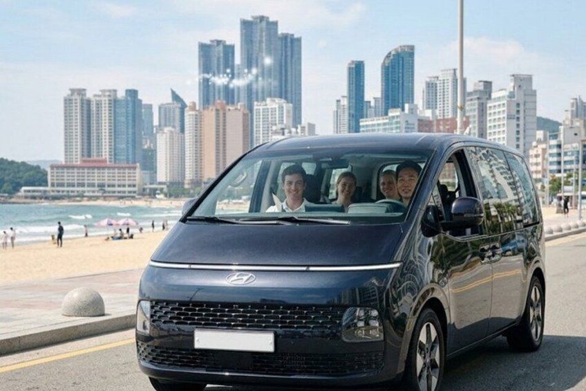 A black van parked on a beach with a city skyline in the background. 1