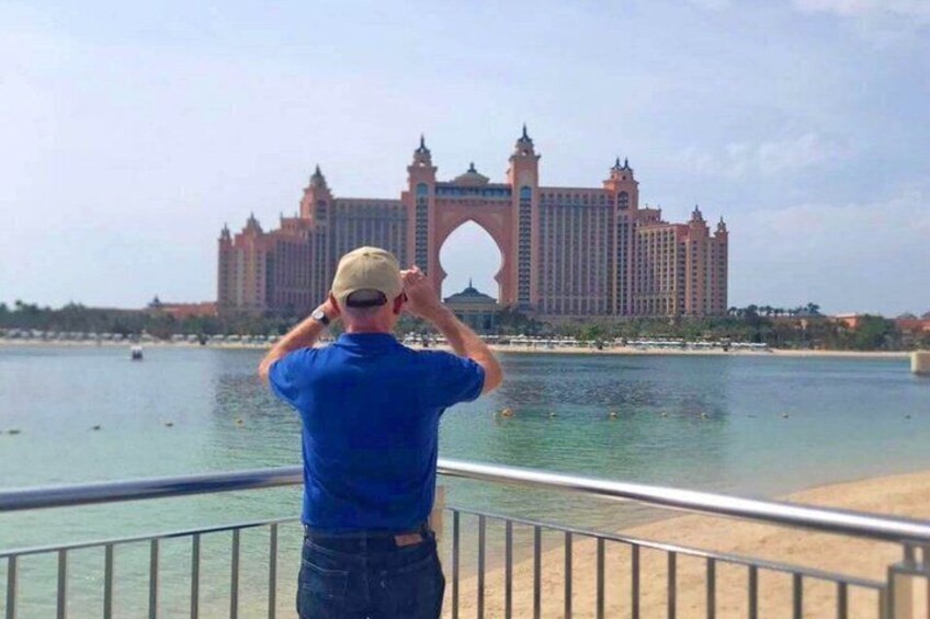 Un hombre fotografiando un hotel grande y ornamentado con un arco distintivo junto al agua. 1