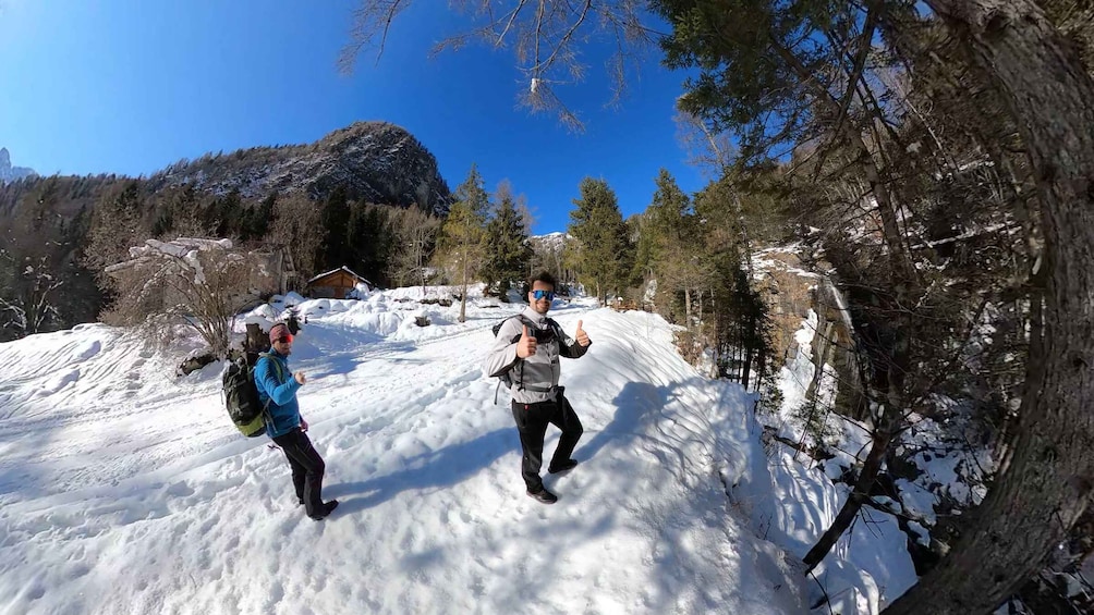 A snowy mountain landscape with two hikers and a cabin in the background. 1