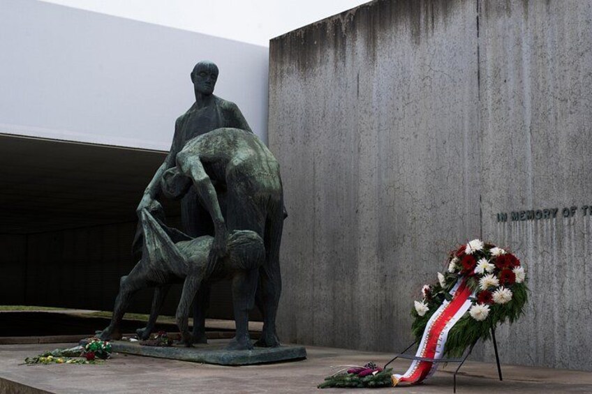 Een bronzen beeld van twee personen, een bloemenkrans en een gedenkplaat. 5
