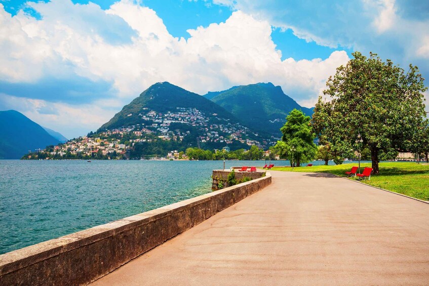 A lakeside walkway with red benches, a mountain in the background, and a clear sky. 5