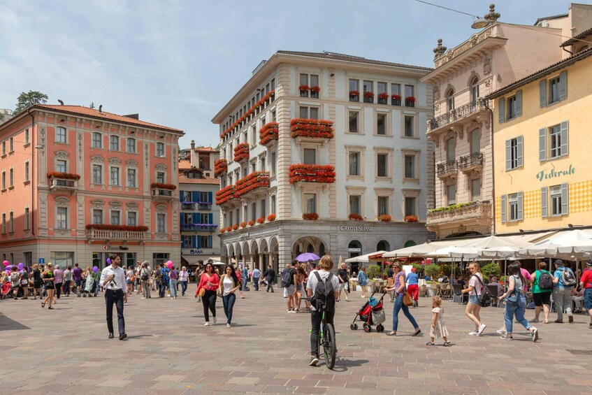 A bustling square with pedestrians, a cyclist, and historic buildings with balconies. 2