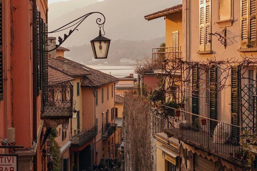 A narrow street with buildings, a street lamp, and a view of a body of water in the distance. 2