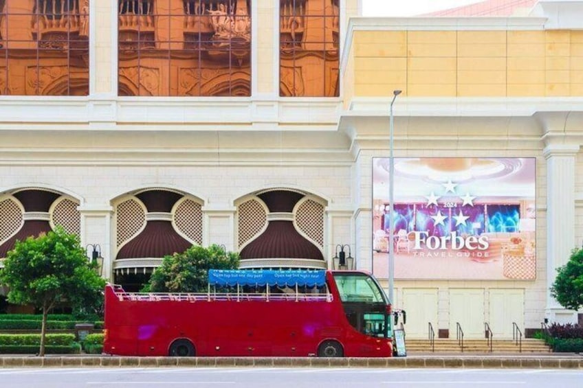 A red bus parked in front of a building with large windows and a Forbes billboard. 2