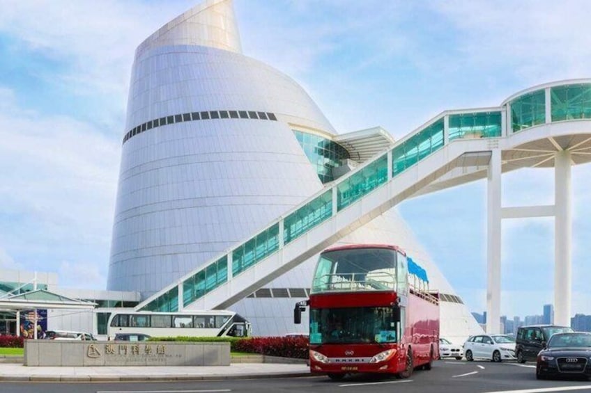 A modern building with a curved facade and a red bus in front. 3