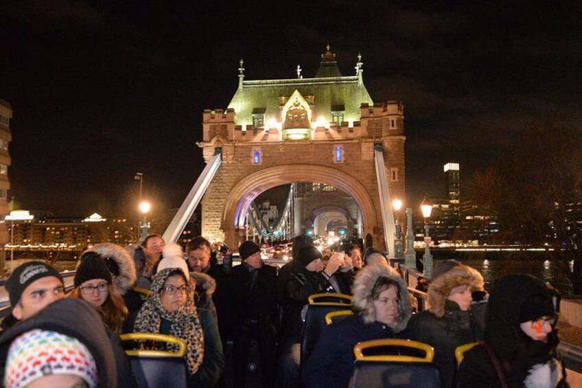 A crowd of people gathered in front of a historic bridge at night. 3