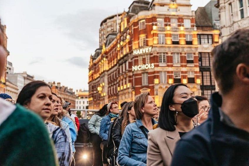 Eine belebte Straße mit Fußgängern, sowie ein Gebäude, auf dem 'HARVEY NICHOLS' steht. 4