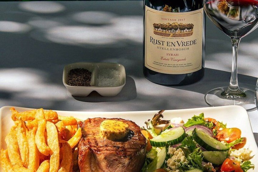 En tallrik med mat, bestående av pommes frites, en grillad biff och en sallad, en flaska vin och ett glas vin på ett bord. 5