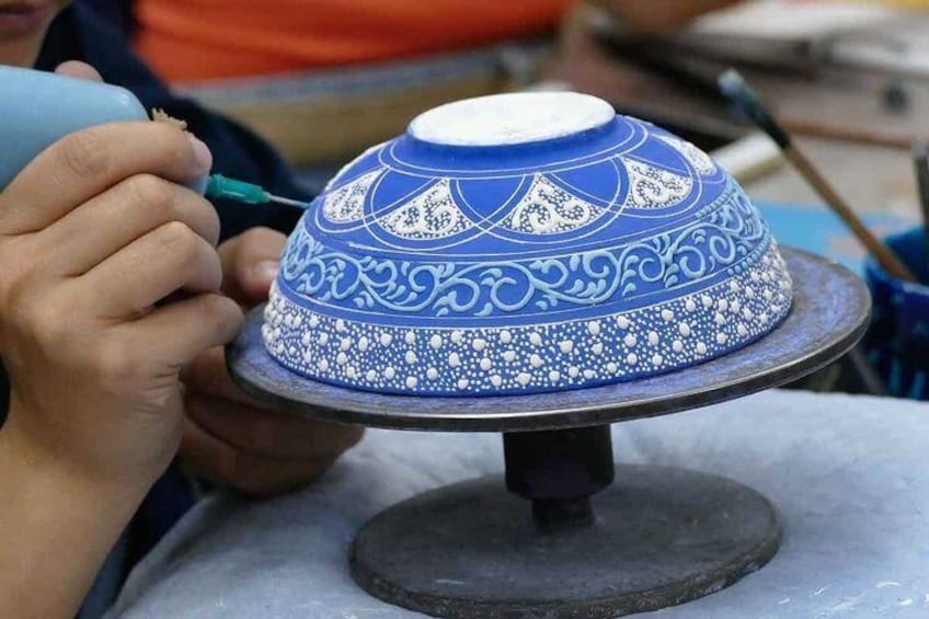 A person painting a blue and white patterned ceramic pot. 5
