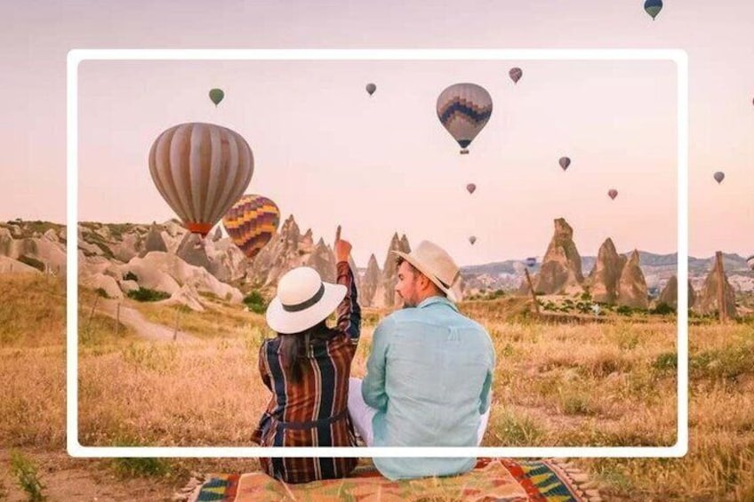 Two people sitting on a blanket, gazing at hot air balloons in a rocky landscape. 3