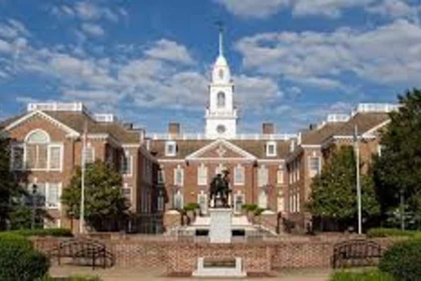 A large brick building with a central tower and a statue in front. 3