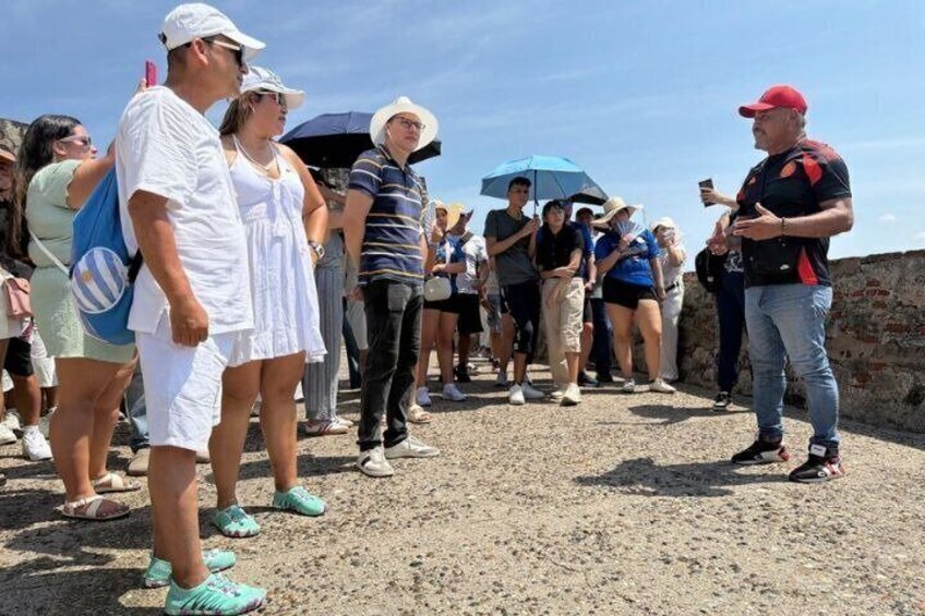 A group of people standing on a sandy area with a brick wall in the background. 1