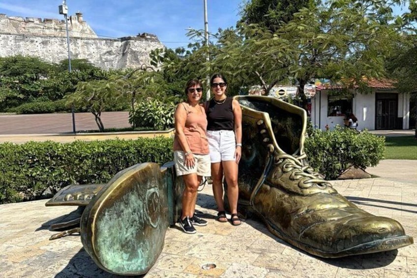 A large bronze shoe sculpture, a person, and a building in the background. 4