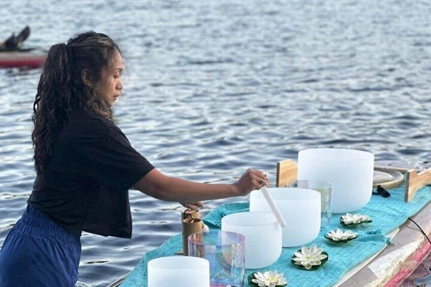 A person on a boat preparing large white containers, possibly for a ritual or ceremony, with a calm sea in the background. 5