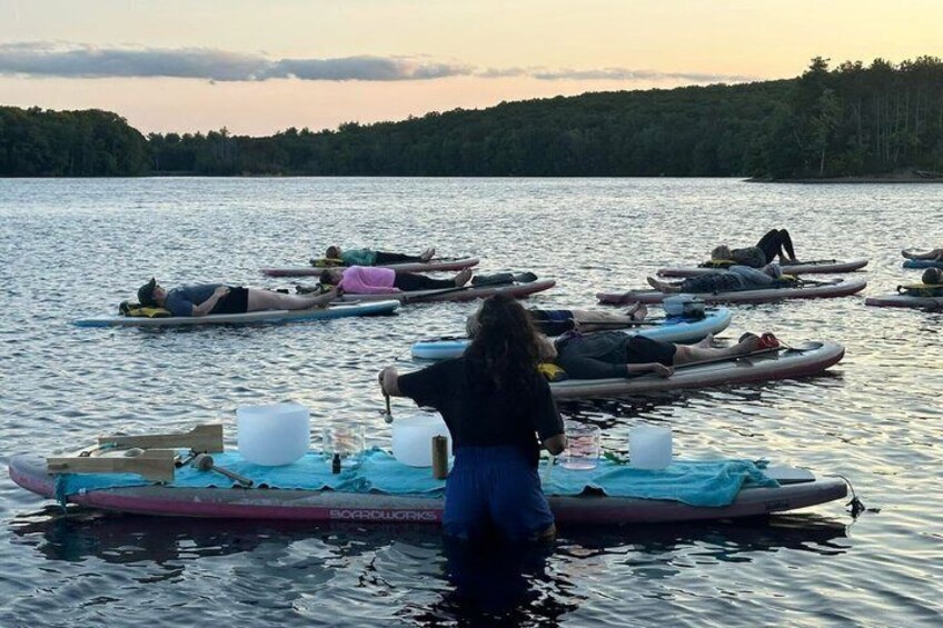 People on kayaks on a calm body of water with trees in the background. 1