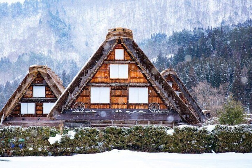 Una cabaña de madera con techo triangular, rodeada de árboles cubiertos de nieve y montañas al fondo. 5