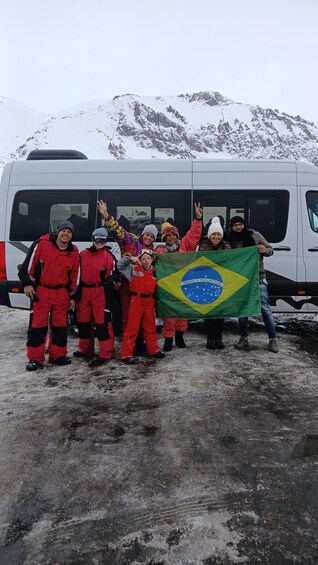 A group of people in red winter gear holding a Brazilian flag in front of a snow-covered mountain and a white bus. 3