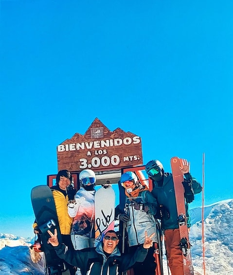 A group of skiers at a mountain summit with a sign reading 'BIENVENIDOS A LOS 3.000 MTS.' 3