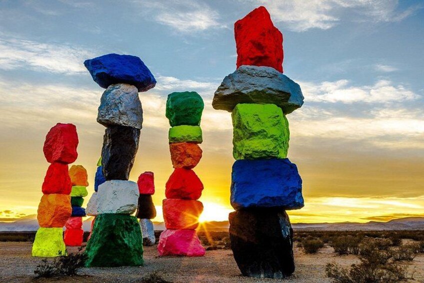 A totem pole with colorful stones stacked vertically against a sunset. 1